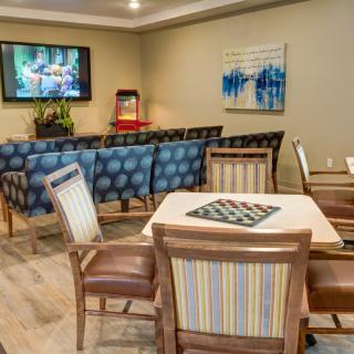 A cozy seating area with a television, artwork on the walls, and comfortable chairs arranged around a table.