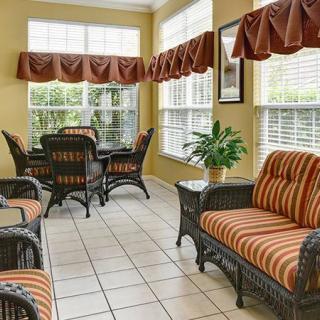 A cozy sunroom with wicker furniture and striped cushions, featuring large windows and a potted plant.