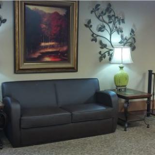 A cozy living room setup with a black sofa, decorative wall art, and a table lamp.