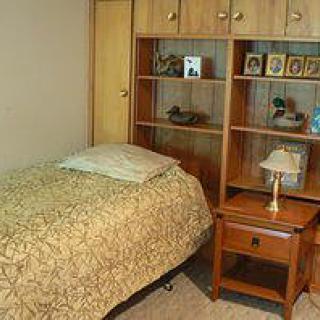 A cozy bedroom with a single bed, wooden nightstand, and shelves adorned with pictures and decor.