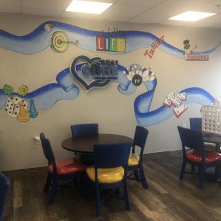 A vibrant mural decorates the wall of a cozy caf space with colorful chairs and round tables.