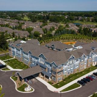 Aerial view of a large, multi-story residential building with landscaped surroundings and a parking lot in a suburban area.