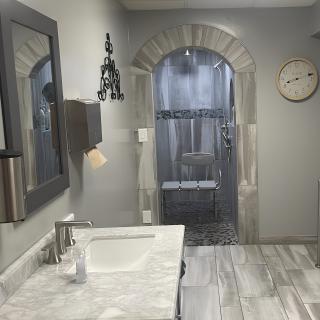 A modern bathroom with a sink, mirror, and shower, featuring gray walls and a decorative arch.
