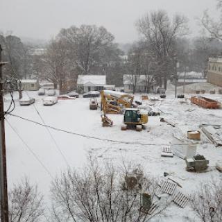 A snowy construction site blanketed in white, with equipment and materials visible amidst the winter landscape.