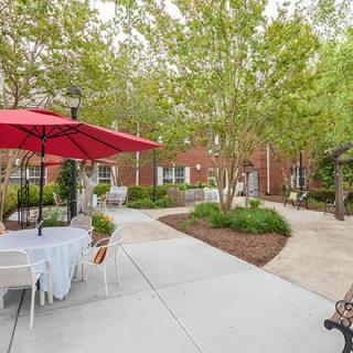 A peaceful outdoor patio with tables and chairs, featuring red umbrellas and surrounded by greenery.