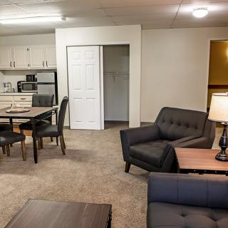 A modern apartment interior featuring a living room area with sofas, a dining table, and an open kitchen space.