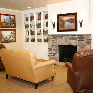 A cozy living room featuring warm armchairs, a stone fireplace, and decorative artwork on the walls.