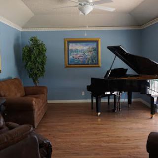 A cozy living room featuring a grand piano, comfortable seating, and a decorative painting.