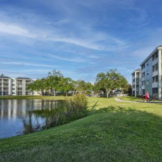 Scenic view of apartment buildings by a tranquil lake under a clear blue sky.