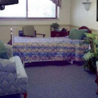 A hospital room with a bed, chair, and floral decorations by the window.