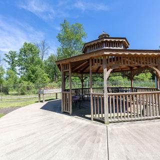 A wooden gazebo in a scenic park setting under a clear blue sky.