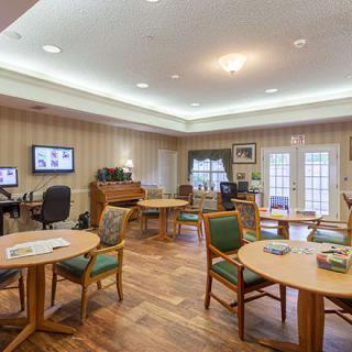 A cozy community room with tables, chairs, a computer station, and a piano.