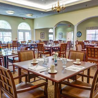 An elegant dining room with neatly arranged tables and chairs, illuminated by a chandelier.