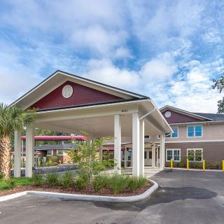 A welcoming entrance to a modern building with prominent columns and well-maintained landscaping under a partly cloudy sky.
