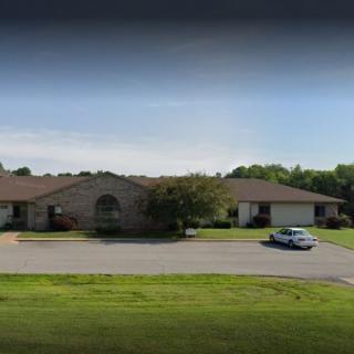 A suburban residential building with a driveway and parked car, surrounded by grass and trees.
