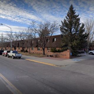 A residential street corner with parked cars and brick townhouses under a partly cloudy sky.