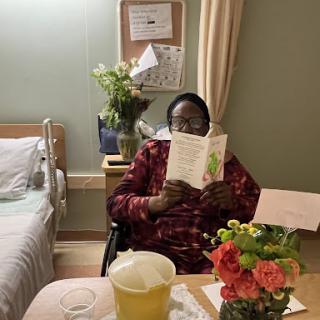 A patient enjoying a book surrounded by flowers in a hospital room.