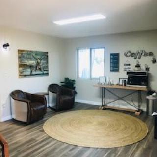 A cozy waiting room with a round rug, modern chairs, and a coffee station.