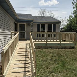 A house with a wooden deck and an accessibility ramp leading to the backyard.