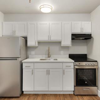 A modern kitchen featuring white cabinets, stainless steel appliances, and a warm hardwood floor.