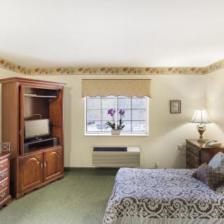 A cozy bedroom with a wooden cabinet, a TV, a large window, and a bed decorated with patterned bedding.