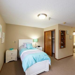 A cozy bedroom with a single bed, nightstand, and closet, featuring soft blue and beige tones.