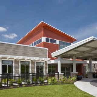 A modern building with large windows and a covered entrance, set against a clear blue sky.