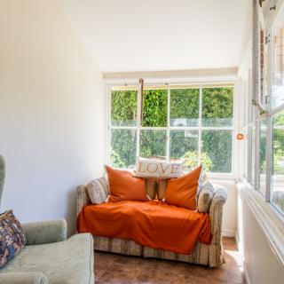 A cozy living room space featuring a sofa with orange cushions, an armchair, and a large window with a view of greenery.