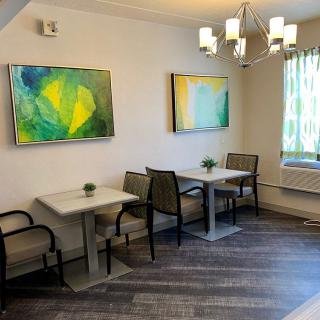 A small dining area with modern artwork, featuring two tables and several chairs under a contemporary chandelier.