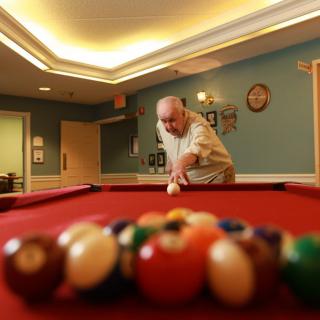 An elderly man playing billiards in a recreation room.