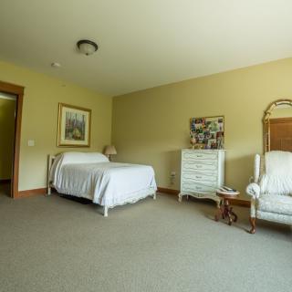 A spacious bedroom with a single bed, upholstered chair, and a white dresser.