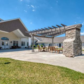 A sunny backyard patio featuring a pergola and stone fireplace.