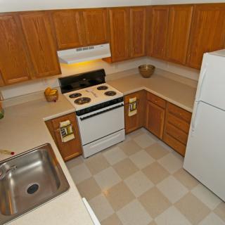 A clean and organized kitchen with wooden cabinets, a stove, sink, and refrigerator.