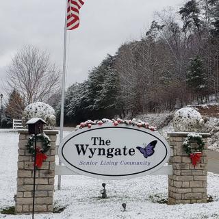 A snowy scene with a sign for The Wyngate, adorned with winter decorations and an American flag.