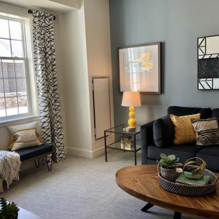 A stylish living room with a cozy sofa, a wooden coffee table, and decorative elements such as artwork, a lamp, and curtains.