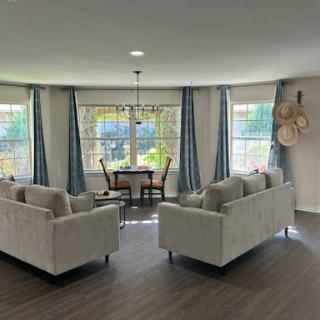 A cozy living room setup featuring comfortable sofas, a dining area with natural light streaming in through the windows.