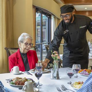 A server in a restaurant is attending to an elderly person enjoying a meal.