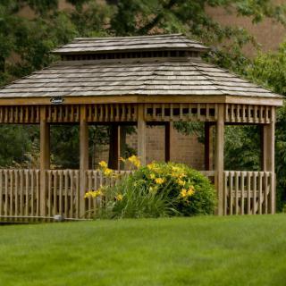 A quaint wooden gazebo surrounded by lush greenery and vibrant flowers.