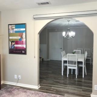 A cozy open-concept living and dining area featuring a stylish arched doorway, bright white furniture, and decorative artwork on the wall.