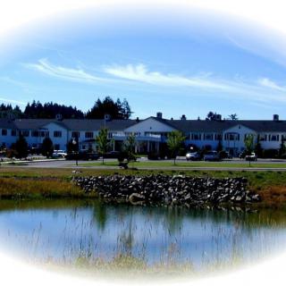 A scenic view of a building with a pond in the foreground, surrounded by nature.