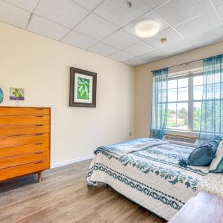 A cozy bedroom with a bed, wooden dresser, and a large window with blue curtains.