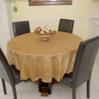 A round dining table with a gold tablecloth and a decorative centerpiece, surrounded by four dark-colored chairs.