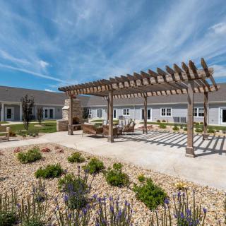 A serene outdoor area featuring a pergola and landscaped garden in front of a building.