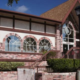 A brick building with large arched windows and a triangular roof under a clear blue sky.