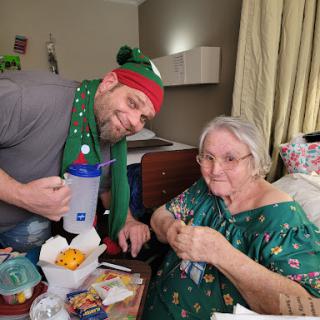 A joyful holiday moment shared between a caregiver and an elderly woman, both dressed in festive attire.