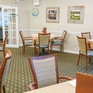 A well-lit dining area with neatly arranged tables and chairs, featuring artwork on the walls and a patterned carpet.