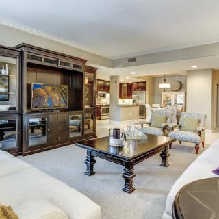 A spacious living room with elegant decor, featuring comfortable seating, a large entertainment unit with a television, and a central coffee table.