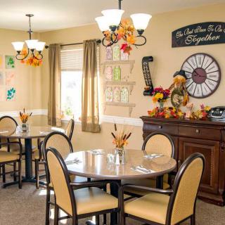 A cozy dining room adorned with autumn-themed decorations, featuring tables set for dining and warm lighting.