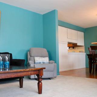 A cozy living room with blue walls, featuring a sofa and coffee table, adjacent to a kitchen and dining area.