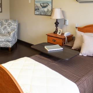 A cozy bedroom featuring a neatly made bed, a nightstand with a lamp, and a comfortable chair.